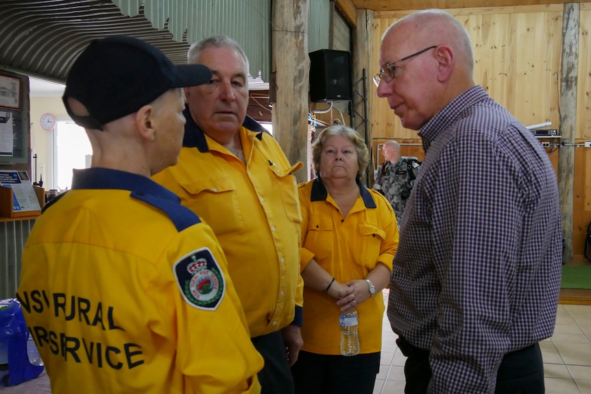 A man talking to a woman and another man who are both in Rural Fire brigade yellow uniforms.
