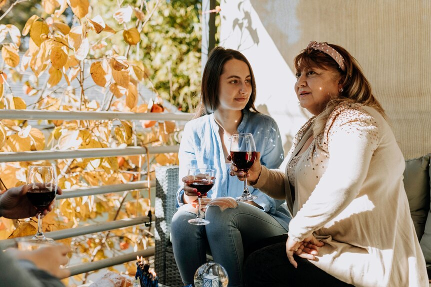 A mother and her young adult daughter drinking red wine.