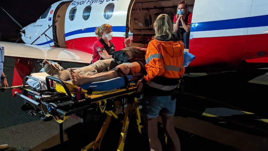 Two women wearing orange high-viz jacket, standing either side of medical stretcher next toRoyal Flying plane.