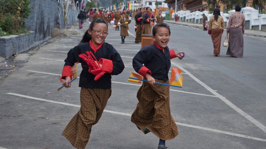 Two children smiling run down the street in Bhutan.