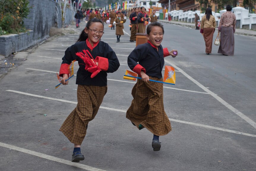 Two children smiling run down the street in Bhutan.