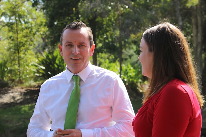 Mark McGowan stands in a bushland setting with Emily Hamilton.