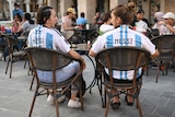 Two women wearing Argentina jerseys with "Messi" on the back sit at an outdoor table