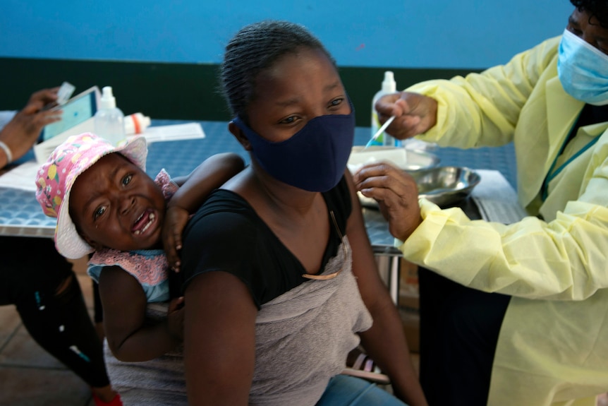 Masked woman receives vaccine with crying baby on her back