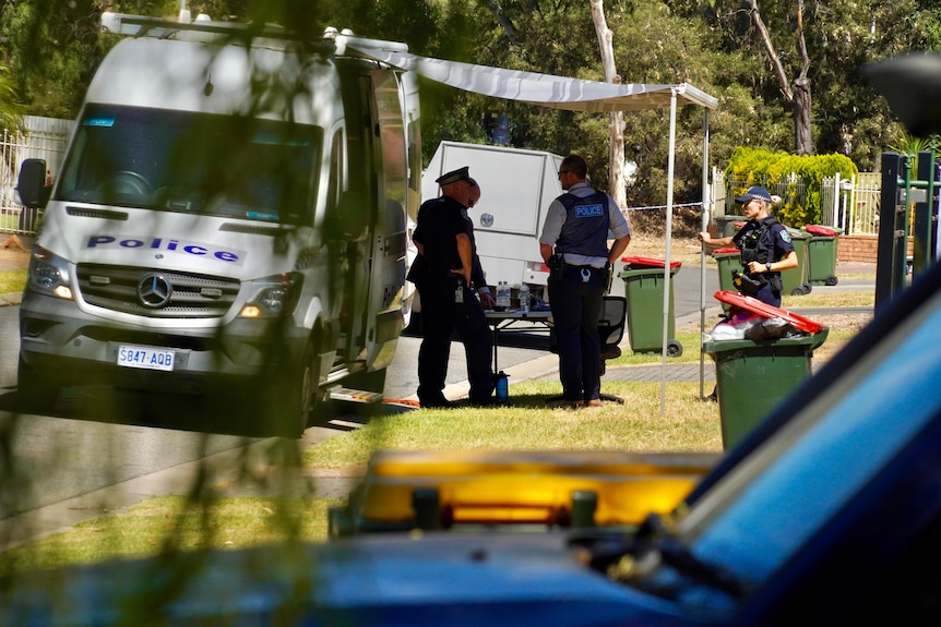 Four police officers stand under an awning attached to a police car, parked on a suburban street