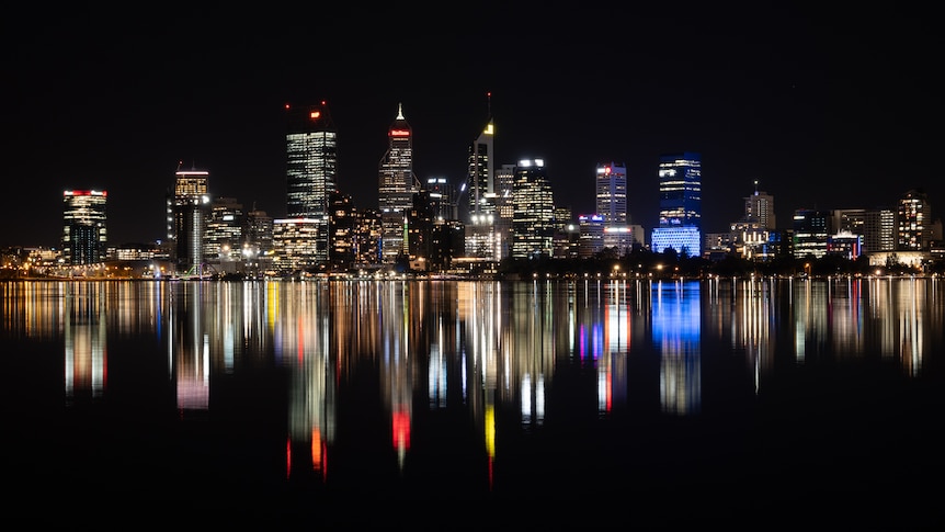 Line of tall brightly lit buildings reflected like a mirror in the surface of the Swan River. 