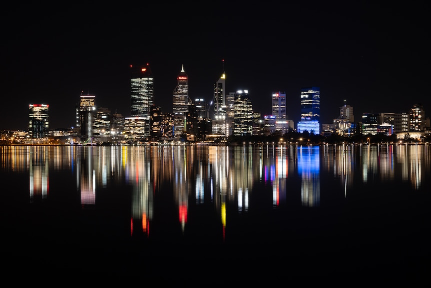 Line of tall brightly lit buildings reflected like a mirror in the surface of the Swan River. 