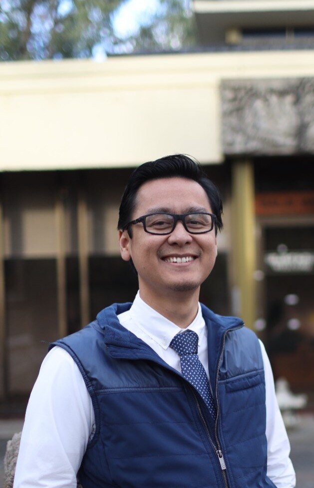a man smiling to the camera wearing a blue vest.