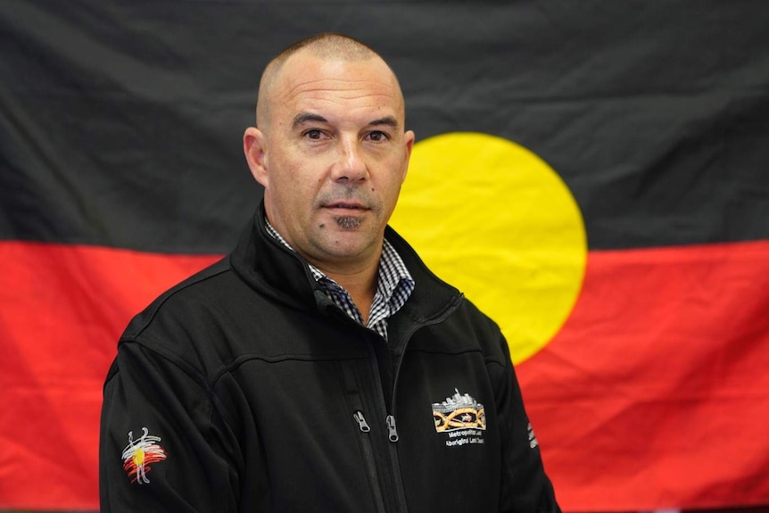 A man stands in front of the Aboriginal flag.