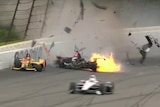 Two cars spin on the track with debris flying in the air behind them with a burst of flame