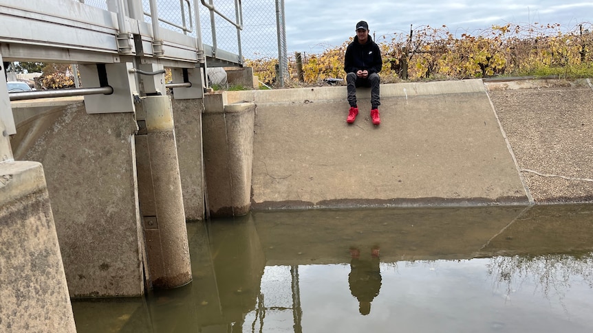Deluca Taylor is sitting on the edge of a concrete irrigation channel and the water level is low