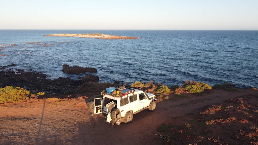 A $WD parked with the back door open on a coastal road next to the ocean.