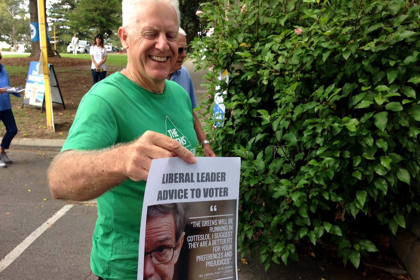 A man in a green t-shirt holds a pamphlet with a photo of the Liberal leader with a quote telling people to vote Greens.