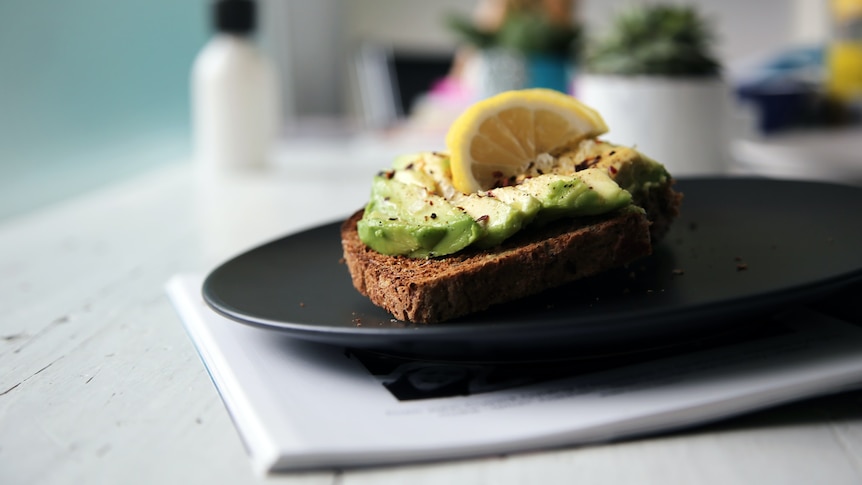 A piece of toast with smashed avocado and a wedge of lemon is served on a plate