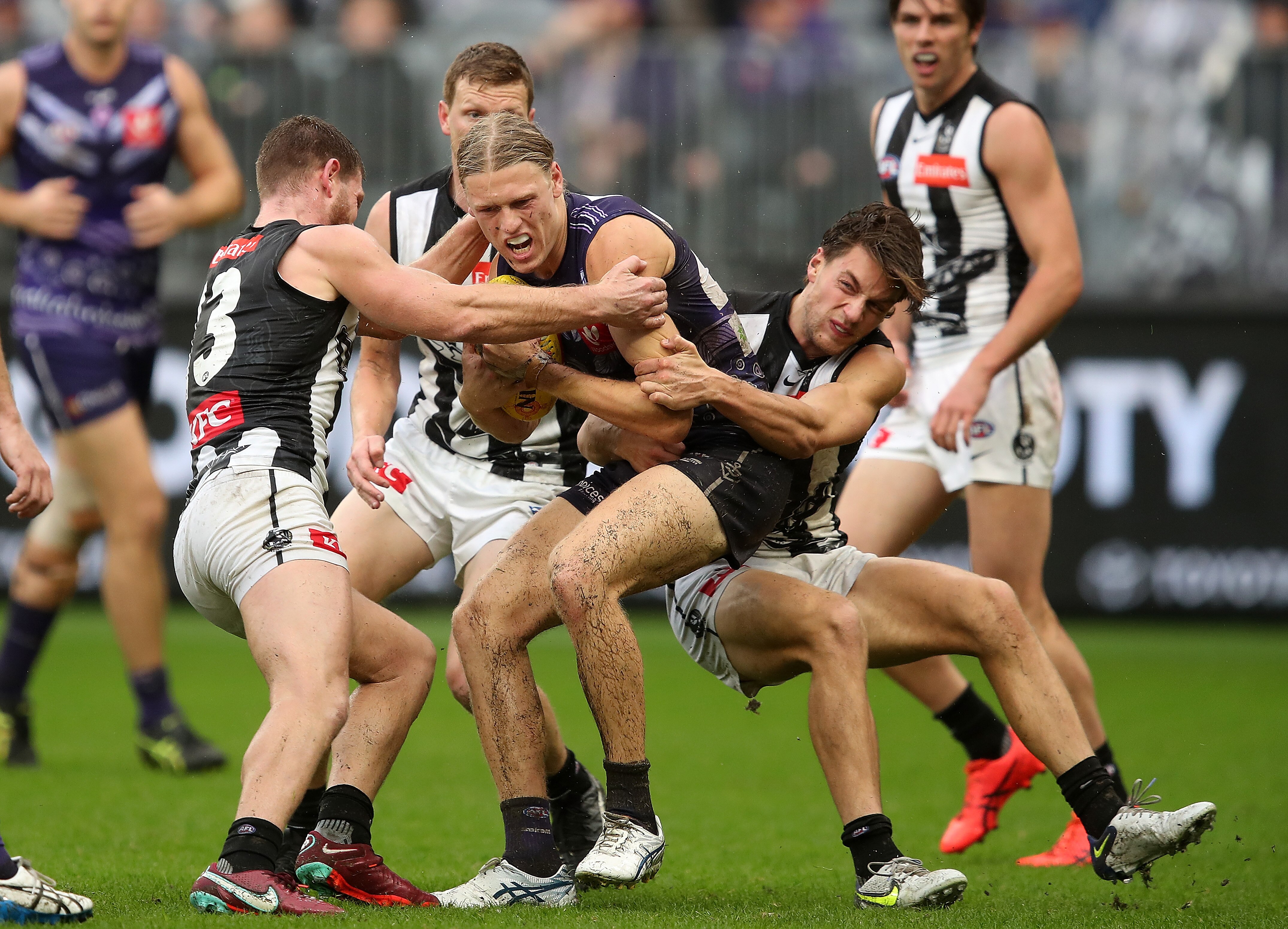A man playing Australian rules football is tackled by a group of players