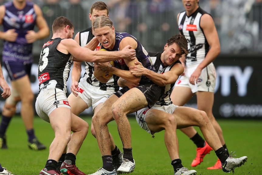 A man playing Australian rules football is tackled by a group of players