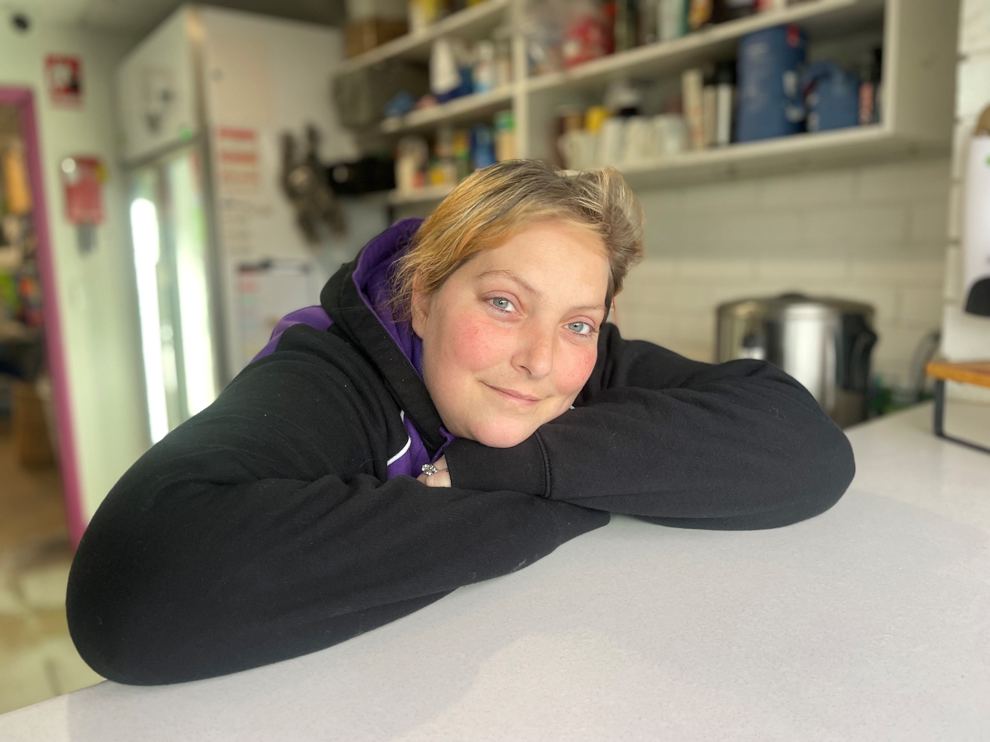 A woman in a black jumper leans on a bench
