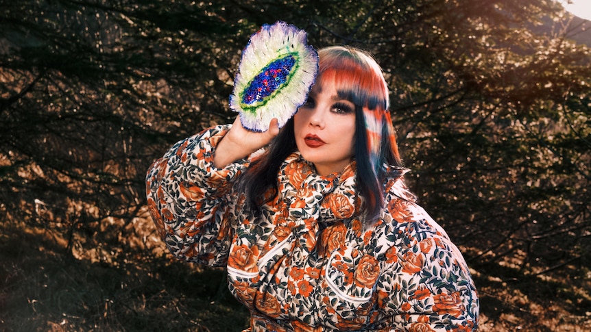 Bjork sits outside on a stool with a mushroom fungus cushion covering one eye