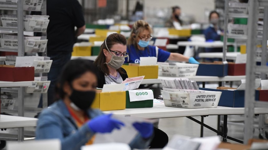 Women working opening envelopes with postal ballots inside in a huge warehouse
