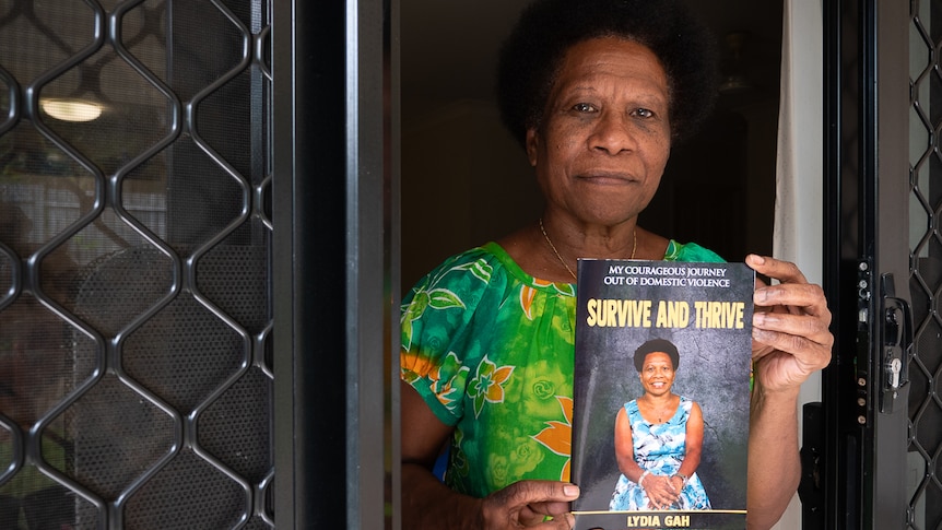 PNG woman standing in doorway holding up autobiography