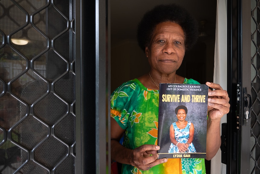 PNG woman standing in doorway holding up autobiography
