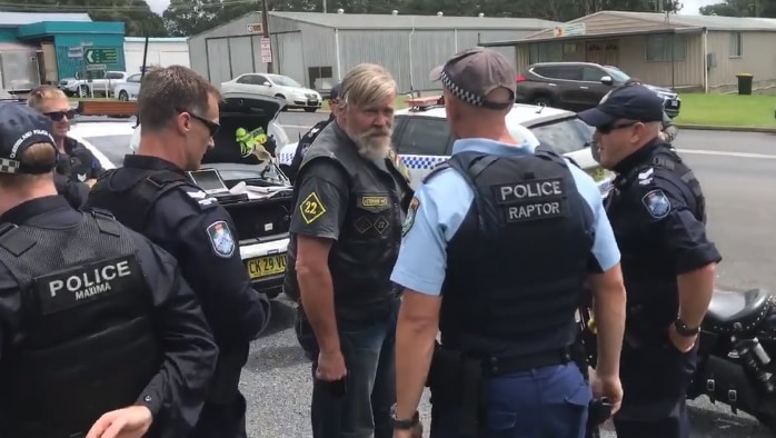 A motorcycle club member speakes to a group of police officers at a roadside stop.
