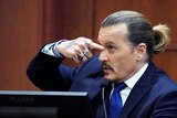 Johnny Depp in the witness stand in a court pointing at his own face. 