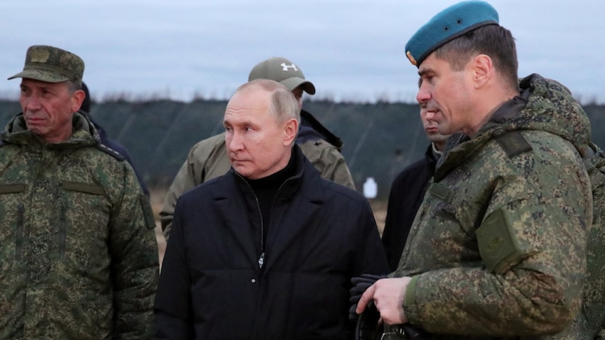 Putin, wearing a black coat, stands flanked by military officials.