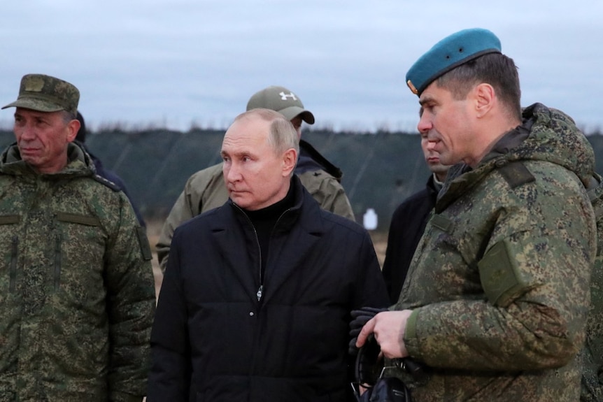 Putin, wearing a black coat, stands flanked by military officials.