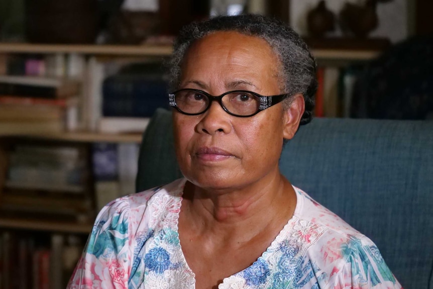 Older woman with black glasses and floral shirt looks at camera.