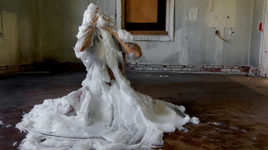 Visual artist Pezaloom is sitting on the floor covered in 160kgs of petroleum jelly.