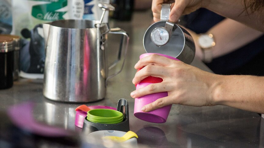 A barista pours milk into a reusable coffee cup