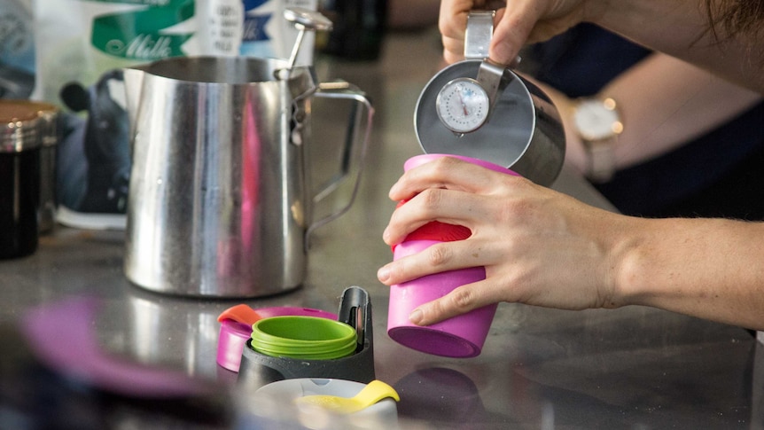 A barista pours milk into a reusable coffee cup