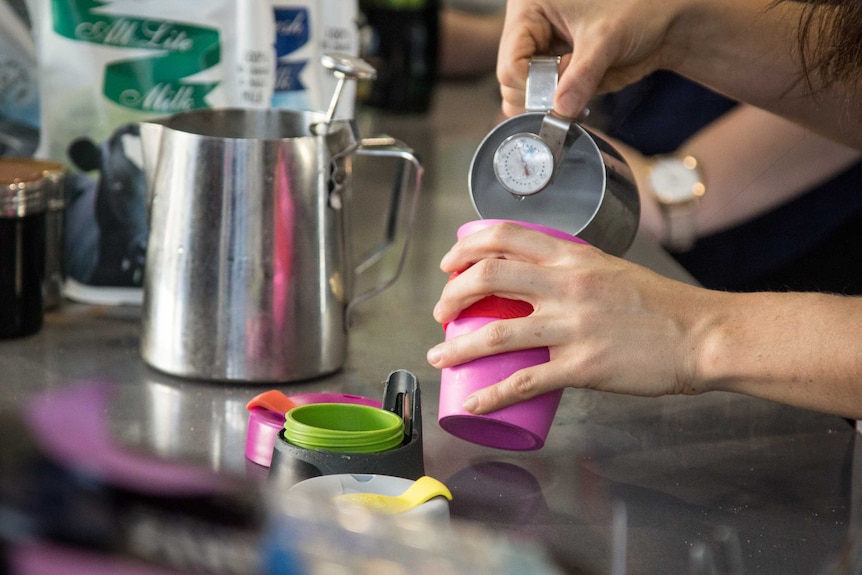 A barista pours milk into a reusable coffee cup