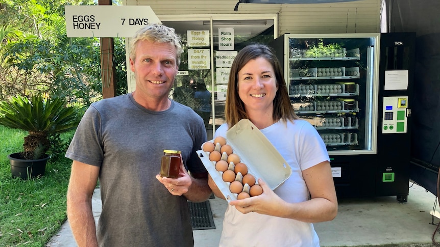 The couple stand in front of a vending machine loaded with eggs and honey.