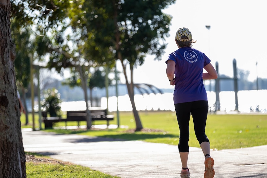 A woman in a parkrun t-shirt runs along a path next to a body of water.