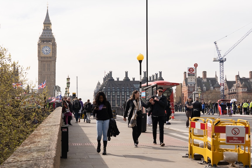 A group of people walk over a bridge with Big Ben in the background.