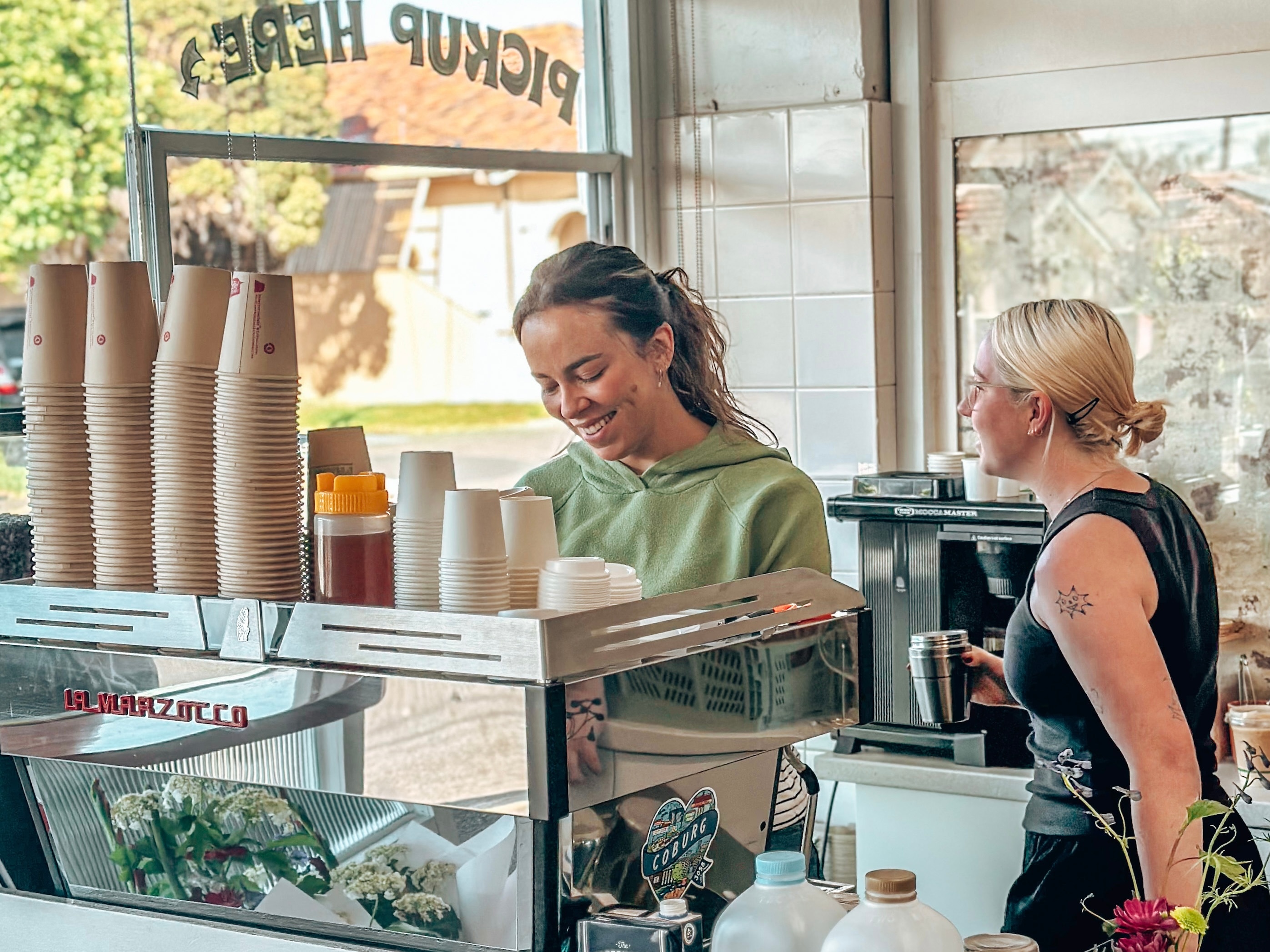 Two women work behind a silver coffee machine of a busy inner city cafe in Melbourne.
