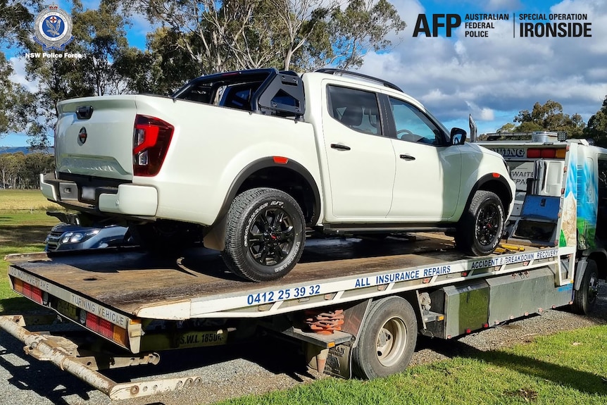 A white ute on the back of a flat bed truck.