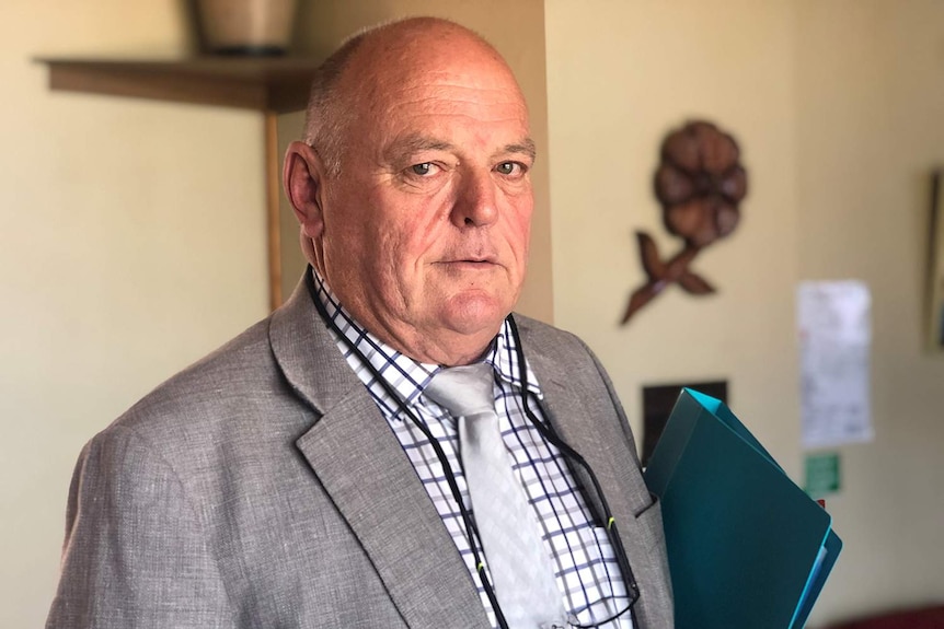 Goondiwindi Mayor Graeme Scheu looks at the camera, holding a folder.