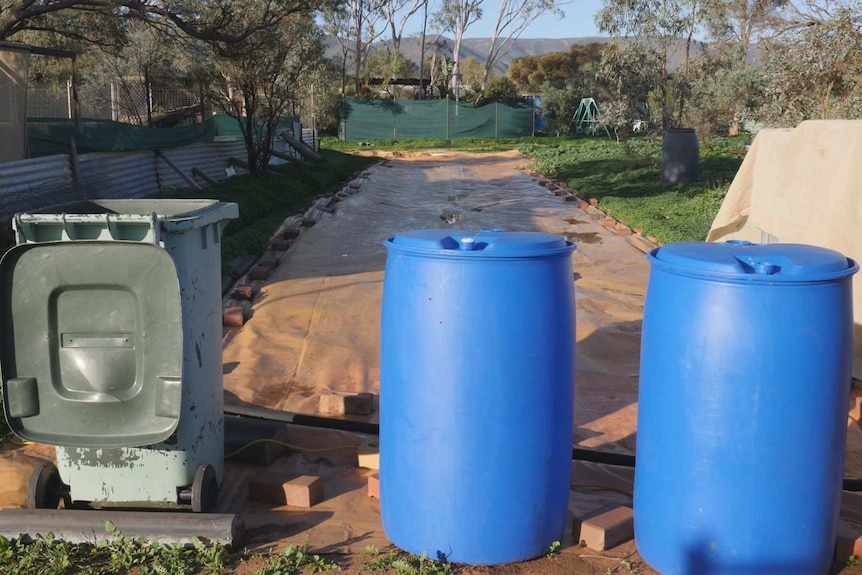 Orange plastic held down by bricks sits on the dirt to direct rainfall into a sump to be pumped into a water tank.