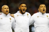 Three english rugby players in national uniform lock arms and sing the national anthem