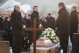 Wide shot of a group of people standing around a coffin being lowered into a grave.