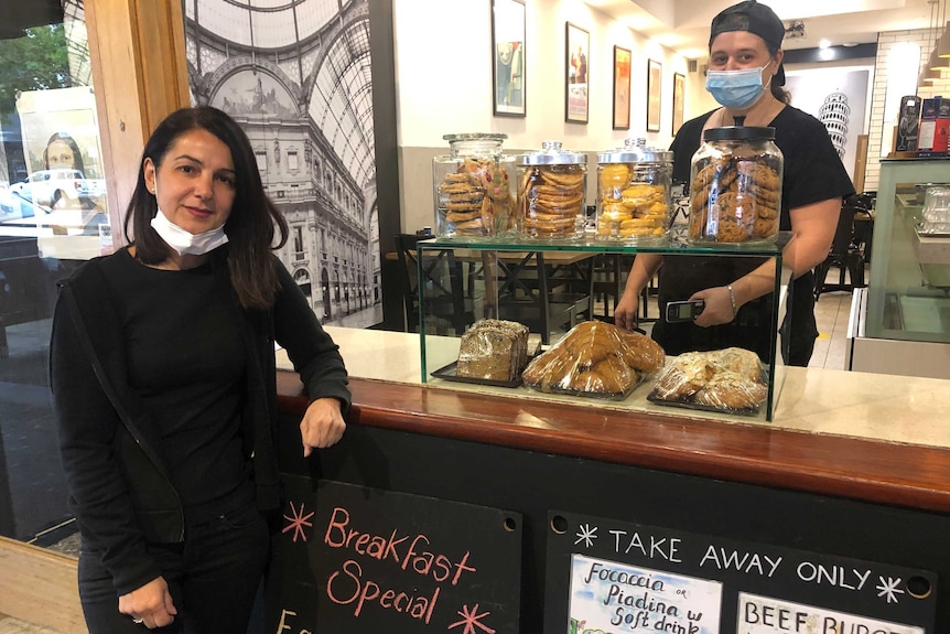 A woman stands next to a sign that says breakfast specials while a worker in a mask stands behind a counter.