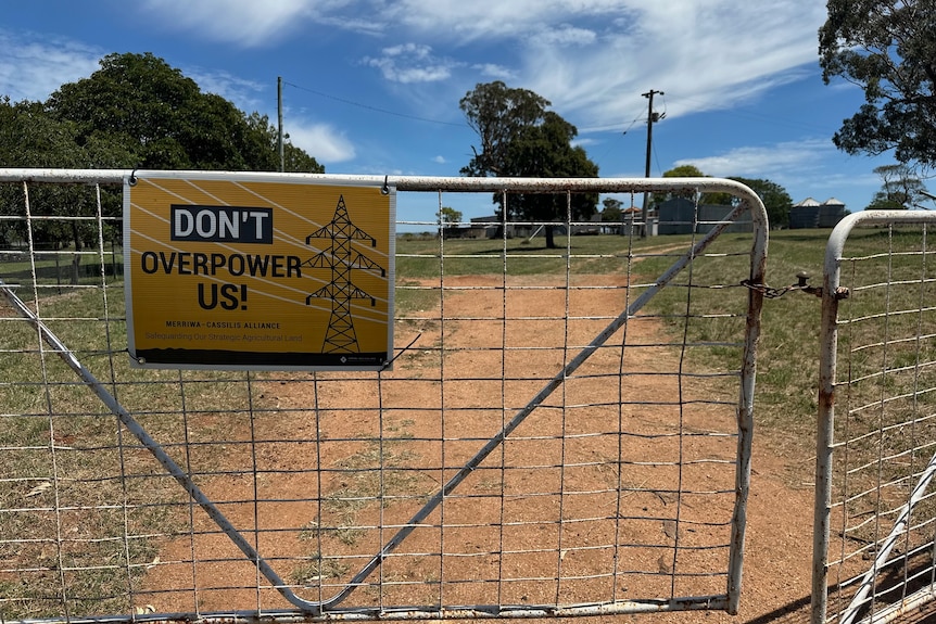 A metal fence on a farm with a sign saying 'Don't Overpower Us!'