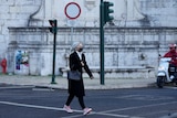 A woman wearing a face mask crosses a street in Lisbon