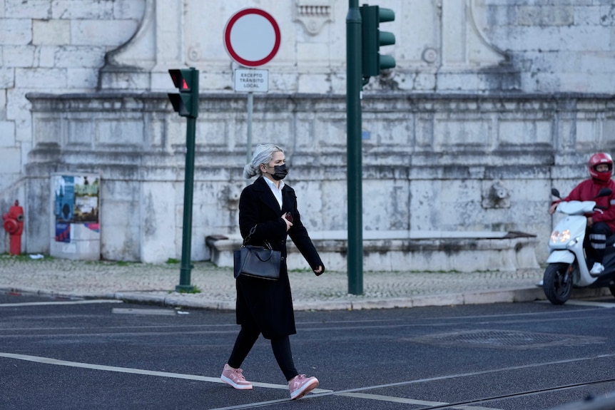 A woman wearing a face mask crosses a street in Lisbon