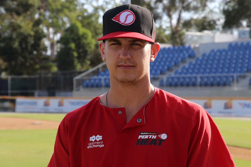 A head and shoulders shot of Perth Heat infielder Robbie Glendinning standing on a baseball field wearing a Heat shirt and hat.