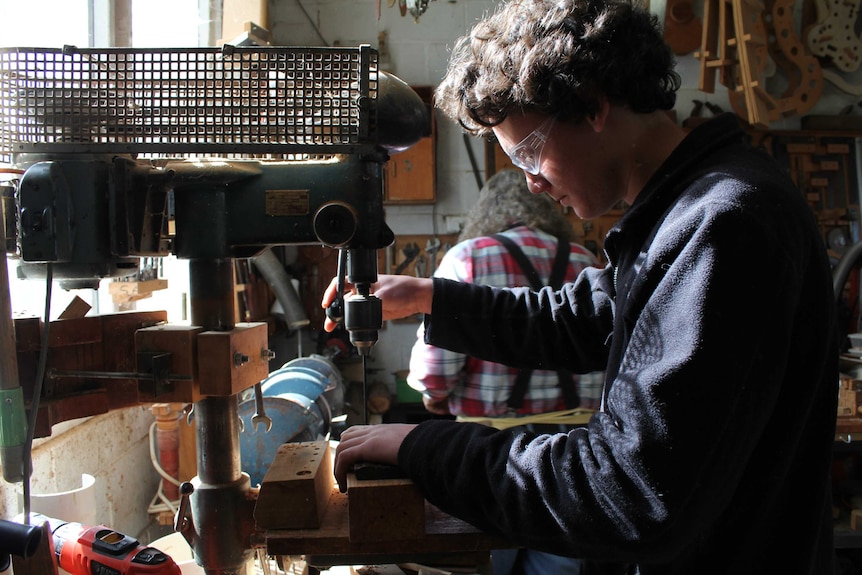 A young man wearing protective goggles works at a mechanical saw.