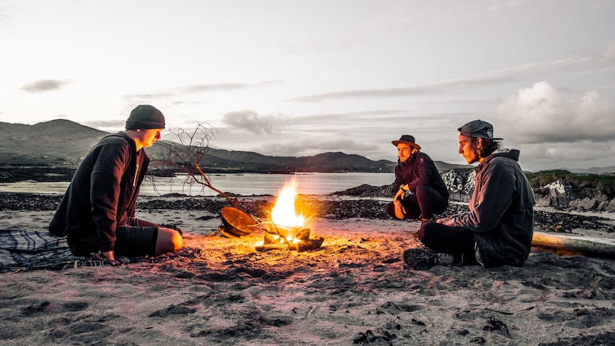 Young men sit around a campfire on a beach for a story about the top causes of burns and scalds and how to avoid them.